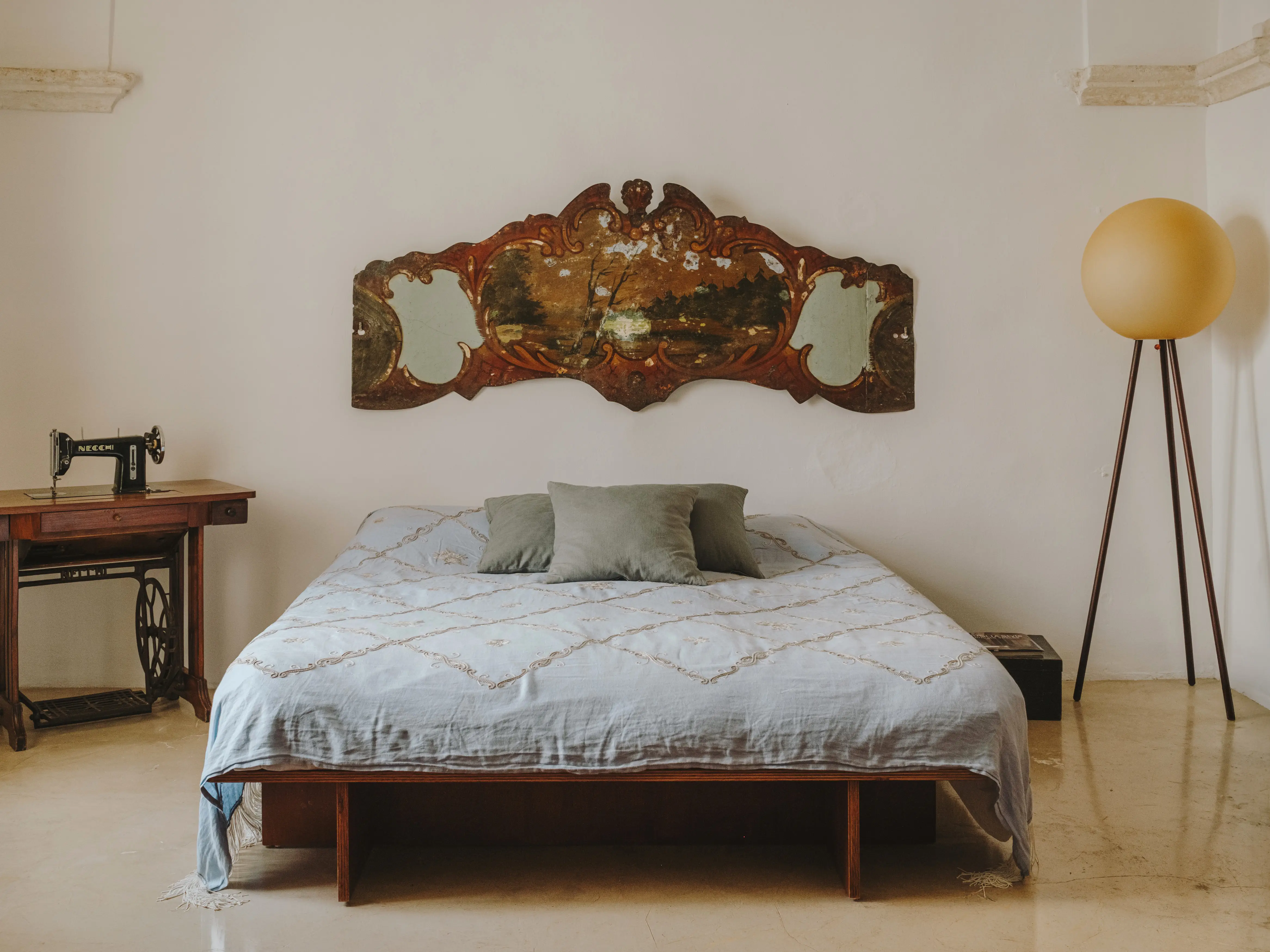 Dormitorio de estilo rústico-chic con cama, cabecero antiguo con espejos, máquina de coser vintage y lámpara de pie esférica.