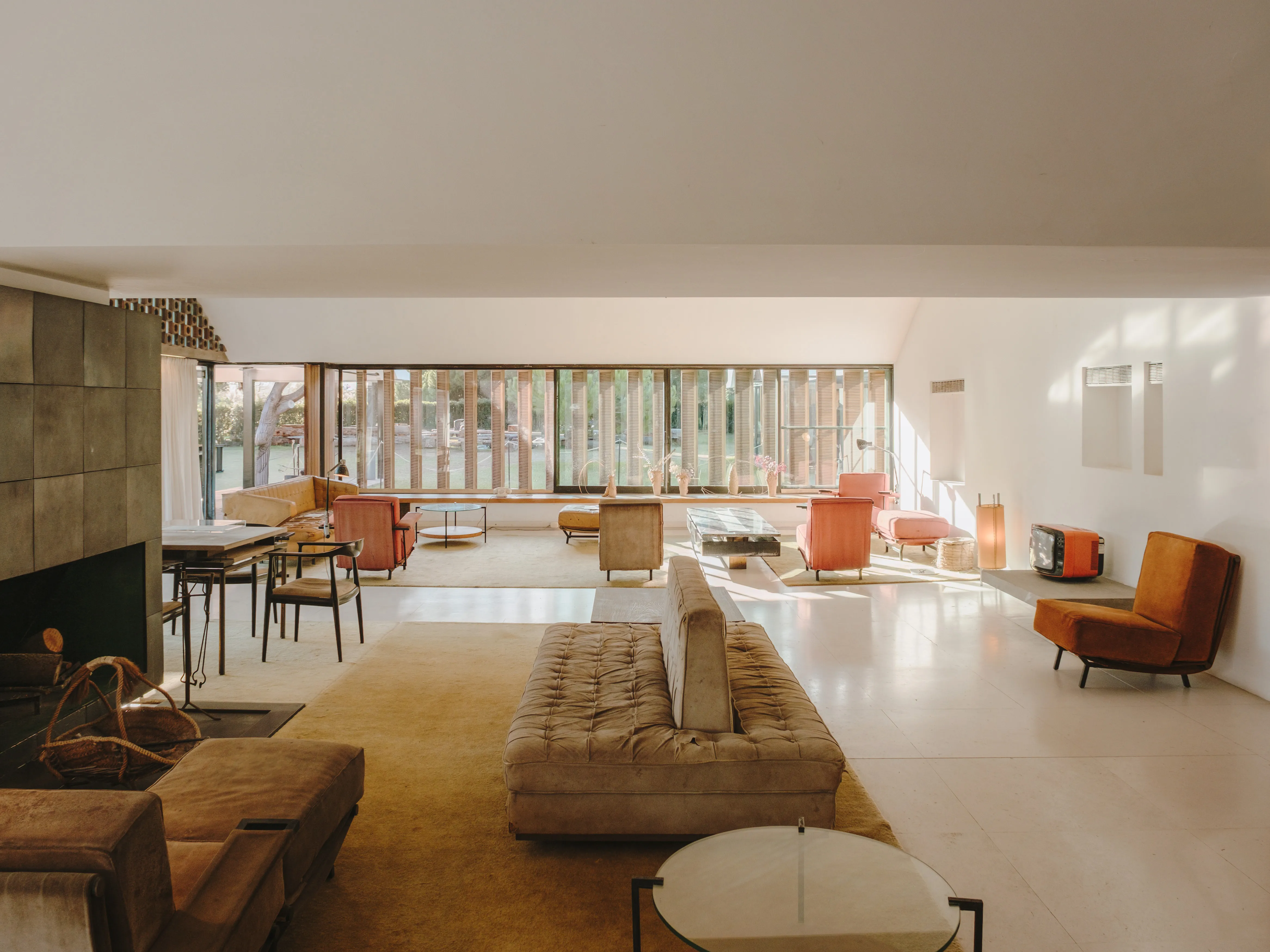 Salón moderno y luminoso con grandes ventanales que dan a un jardín, destacando mobiliario contemporáneo y una chimenea.